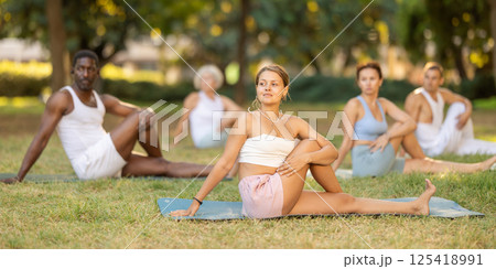 Girl performing Vakrasana during group yoga session outdoors 125418991