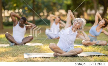 Multinational yoga enthusiasts with senior female coach perform padmasana in park 125419004