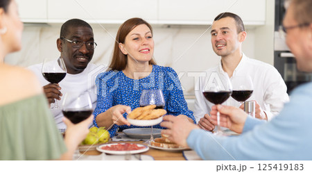 Companions congregated around a festive table, participating in animated discussions and enjoying the delights of red wine Companions congregated around a festive table, participating in animated discussions and enjoying the delights of red wine 125419183