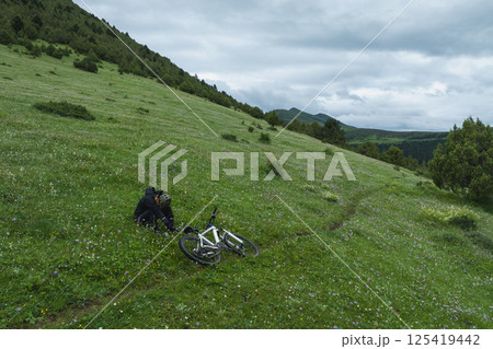 Aerial view of woman riding mountain bike on flowering grassland mountain trail 125419442