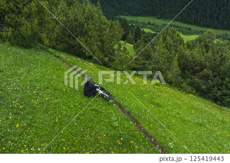 Aerial view of woman riding mountain bike on flowering grassland mountain trail 125419443
