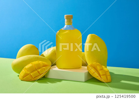A bottle of mango juice on a rectangular podium, surrounded by a jumble of ripe mangoes. The mangoes had thin skin, cut in half and scored into squares. Alphonso mango fruit have many vitamins. A bottle of mango juice on a rectangular podium, surrounded by a jumble of ripe mangoes. The mangoes had thin skin, cut in half and scored into squares. Alphonso mango fruit have many vitamins. 125419500