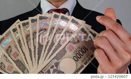 沢山の新一万円札を持ちポーズをするビジネスマン	 125420607