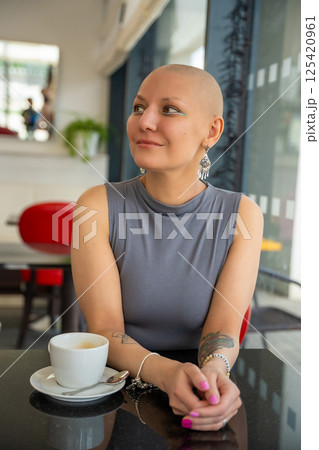 Confident young woman with cancer enjoying coffee in a cafe, embracing life despite illness. The concept shows that a cancer diagnosis does not take away the ability to enjoy normal activities 125420961