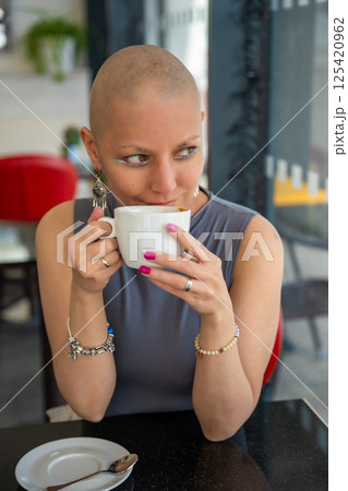 Confident young woman with cancer enjoying coffee in a cafe, embracing life despite illness. The concept shows that a cancer diagnosis does not take away the ability to enjoy normal activities 125420962