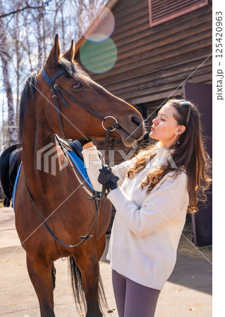 Young woman standing beside a horse at a stable. Concept of emotional connection between humans and animals. 125420963