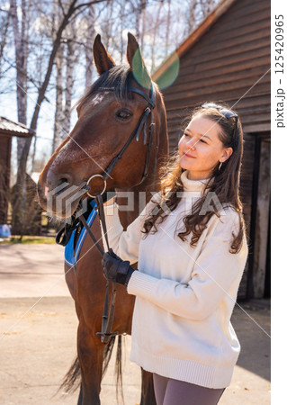 Young woman standing beside a horse at a stable. Concept of emotional connection between humans and animals. 125420965