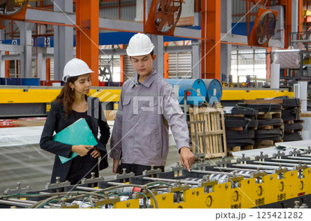 Two worker with safety helmet and black suit standing in a factory, holding clipboard, used for taking note, check schedule and review document. Two worker with safety helmet and black suit standing in a factory, holding clipboard, used for taking note, check schedule and review document. 125421282