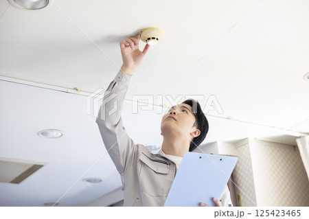 ビルメンテナンス　火災報知器を点検する作業着姿の男性 125423465