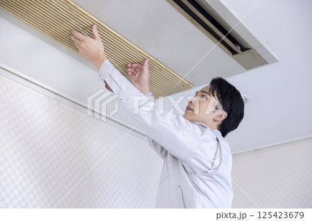 ビルメンテナンス　エアコンの点検をする作業着姿の男性 125423679