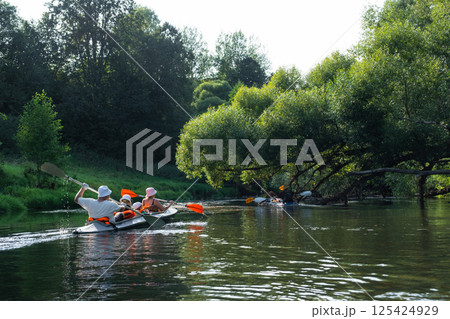Family with children on rafting trip in Group kayak trip of different ages, adults, elderly. Rowing boat on the river, a water hike, summer adventure. 125424929