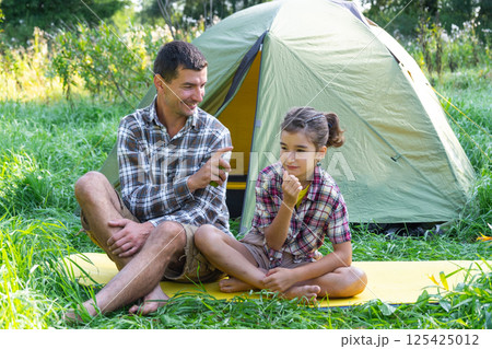 Dad sprays repellent on daughter outdoor camping and picnicking near a tent Dad sprays repellent on daughter outdoor camping and picnicking near a tent 125425012