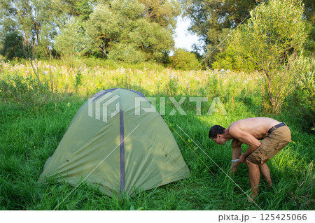 The man installs and assembles tourist tent in a camping in nature in the forest. Domestic tourism, active summer holidays, family adventures. Ecotourism, sport, hike The man installs and assembles tourist tent in a camping in nature in the forest. Domestic tourism, active summer holidays, family adventures. Ecotourism, sport, hike 125425066