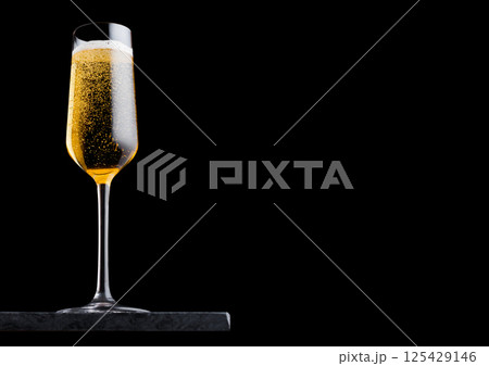 Elegant glass of yellow champagne with bubbles on blavk marble board on black background. 125429146