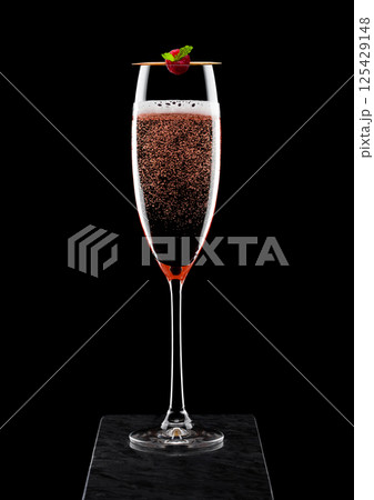 Elegant glass of pink rose champagne with raspberry on stick on black marble board on black 125429148