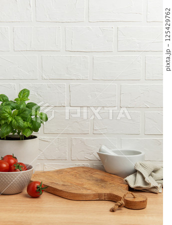 Kitchen utensils, fresh tomatoes, basil plant and mortar with pestle on wooden table Kitchen utensils, fresh tomatoes, basil plant and mortar with pestle on wooden table 125429762