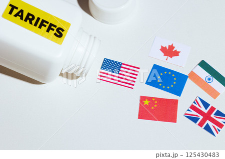 Tariff-labeled pill bottle spilling global trade flags 125430483
