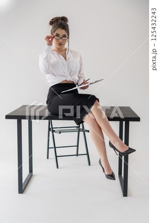 Stylish businesswoman sitting on desk with papers, looking at camera with confident expression 125432243