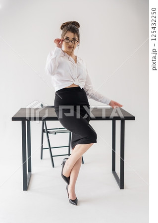 Young business woman adjusting glasses while leaning on dark table in modern office setting 125432250