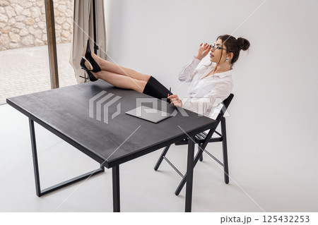 Relaxed businesswoman propped feet on a desk while writing and looking down in a modern office space 125432253