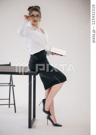 Stylish businesswoman leaning against a table with a book in a modern office setting Stylish businesswoman leaning against a table with a book in a modern office setting 125432319