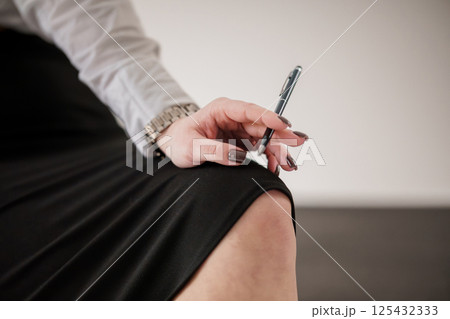 Businesswoman holding a pen and sitting in a black skirt with a watch Businesswoman holding a pen and sitting in a black skirt with a watch 125432333