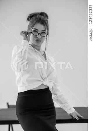 Stylish young woman in white shirt and black skirt posing indoors with glasses Stylish young woman in white shirt and black skirt posing indoors with glasses 125432337