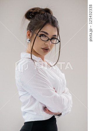 Portrait of a confident young woman in formal attire with glasses, arms crossed and serious expression Portrait of a confident young woman in formal attire with glasses, arms crossed and serious expression 125432338
