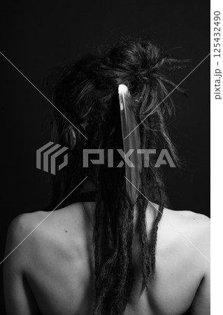 Studio portrait of woman with long dreadlocks and big feather in her hair standing back to camera Studio portrait of woman with long dreadlocks and big feather in her hair standing back to camera 125432490