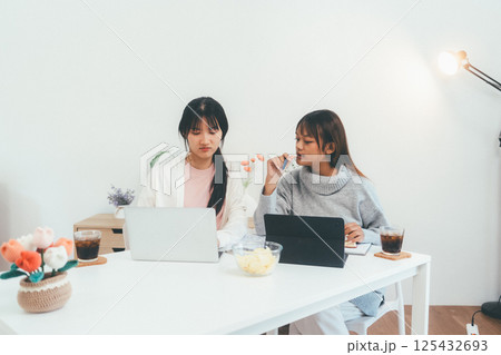 Female higher education student using laptop and studying book in home, Online learning. Female higher education student using laptop and studying book in home, Online learning. 125432693