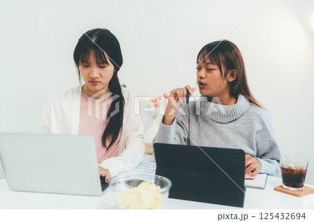 Female higher education student using laptop and studying book in home, Online learning. Female higher education student using laptop and studying book in home, Online learning. 125432694