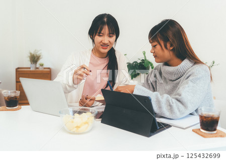 Female higher education student using laptop and studying book in home, Online learning. Female higher education student using laptop and studying book in home, Online learning. 125432699