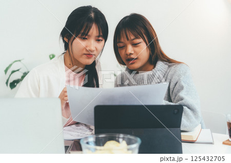 Female higher education student using laptop and studying book in home, Online learning. 125432705