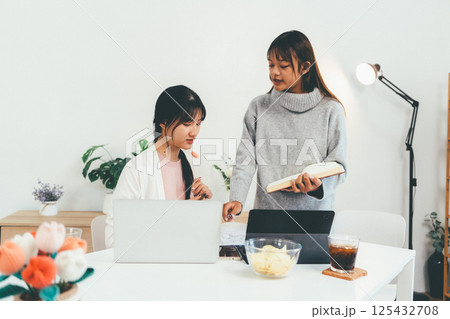 Female higher education student using laptop and studying book in home, Online learning. Female higher education student using laptop and studying book in home, Online learning. 125432708