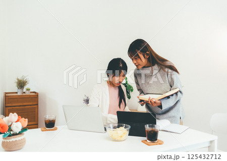 Female higher education student using laptop and studying book in home, Online learning. 125432712