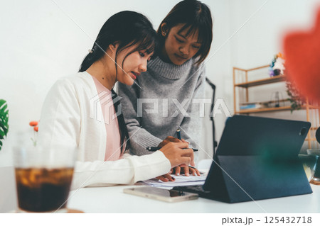 Female higher education student using laptop and studying book in home, Online learning. 125432718