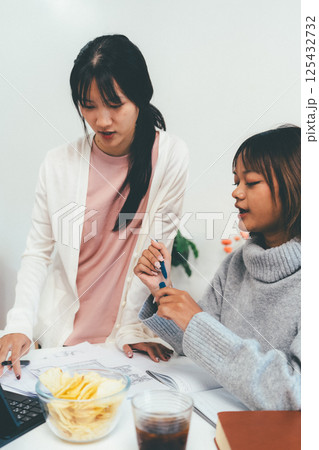 Female higher education student using laptop and studying book in home, Online learning. Female higher education student using laptop and studying book in home, Online learning. 125432732