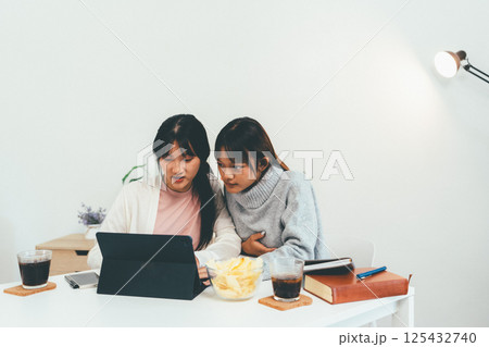 Female higher education student using laptop and studying book in home, Online learning. Female higher education student using laptop and studying book in home, Online learning. 125432740