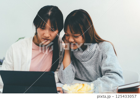 Female higher education student using laptop and studying book in home, Online learning. 125433057