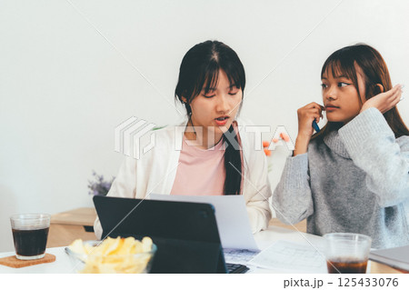 Female higher education student using laptop and studying book in home, Online learning. Female higher education student using laptop and studying book in home, Online learning. 125433076