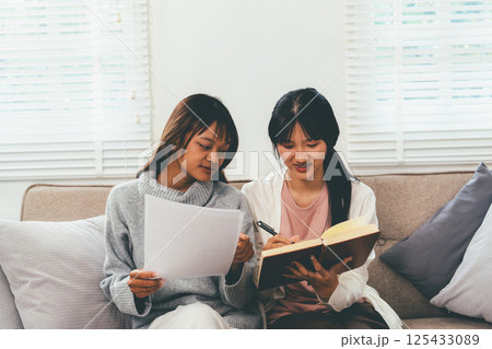 Female higher education student using laptop and studying book in home, Online learning. 125433089