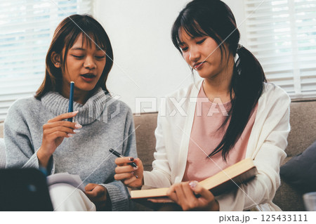 Female higher education student using laptop and studying book in home, Online learning. Female higher education student using laptop and studying book in home, Online learning. 125433111