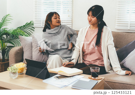 Female higher education student using laptop and studying book in home, Online learning. Female higher education student using laptop and studying book in home, Online learning. 125433121