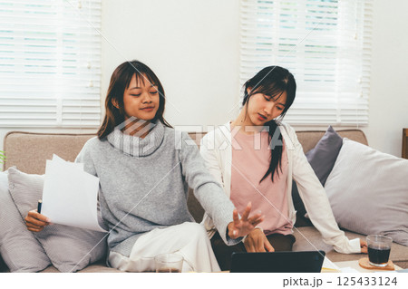 Female higher education student using laptop and studying book in home, Online learning. 125433124