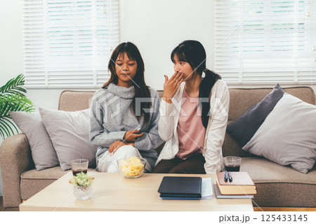 Female higher education student using laptop and studying book in home, Online learning. 125433145