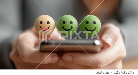 person holding phone with three floating smiley emoticons, expressing positivity 125433278