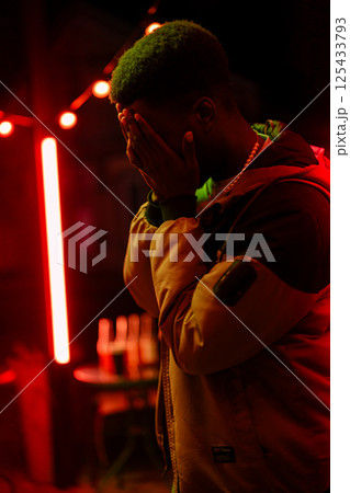 Emotional moment captured at night in a vibrant urban setting with red lights and a contemplative figure Emotional moment captured at night in a vibrant urban setting with red lights and a contemplative figure 125433793