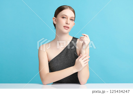A beautiful young woman with clean, fresh skin against a blue background. Skincare, facial treatment, cosmetology, beauty, and spa. An elegant portrait of an woman. 125434247