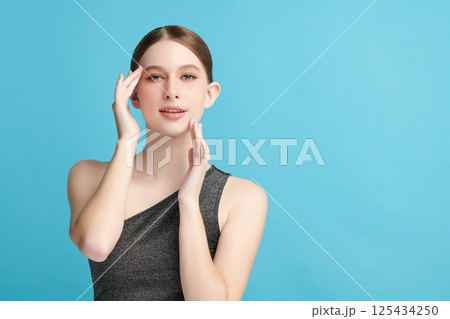 A beautiful young woman with clean, fresh skin against a blue background. Skincare, facial treatment, cosmetology, beauty, and spa. An elegant portrait of an woman. 125434250