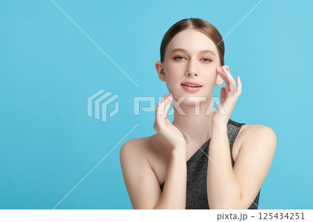 A beautiful young woman with clean, fresh skin against a blue background. Skincare, facial treatment, cosmetology, beauty, and spa. An elegant portrait of an woman. 125434251